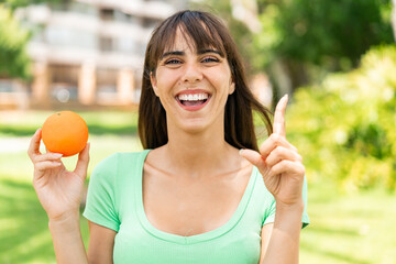 Young woman holding an orange at outdoors pointing up a great idea