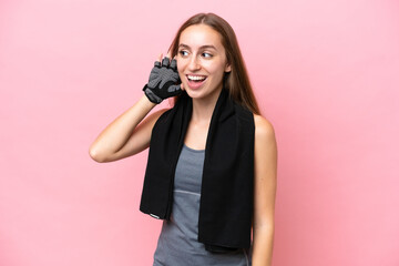 Young sport caucasian woman wearing a towel isolated on pink background listening to something by putting hand on the ear