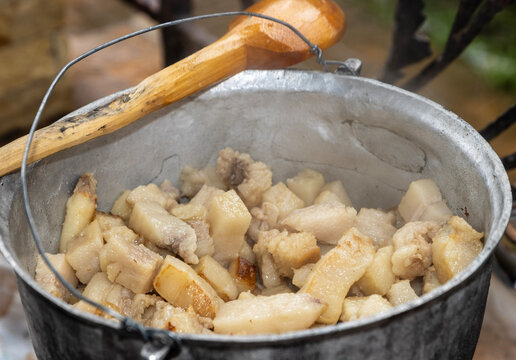 A cauldron filled with "jumări", a traditional Romanian dish made from rendered pork fat. Its interior is filled with irregularly shaped pieces of pork fat in various stages of exhaustion.