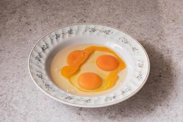 Raw eggs with yolks and whites in a floral-decorated ceramic bowl, placed on a marble kitchen counter