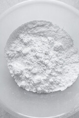 Overhead view of icing sugar in a bowl, top view of powdered sugar on a marble countertop