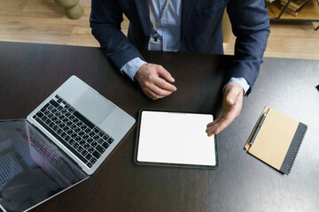 Fototapeta premium Man is sitting at a desk with a laptop and a tablet. The tablet is open to a blank screen