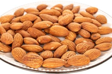 Fragrant roasted almonds in a ceramic saucer, close-up, isolated on a white background.