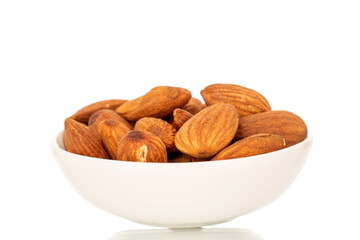 Fragrant roasted almonds in a ceramic saucer, close-up, isolated on a white background.