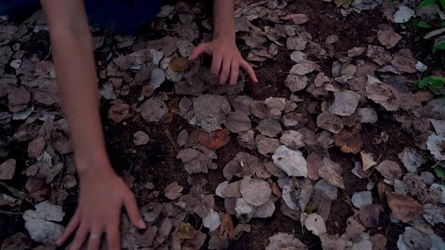 Chica joven sentada en un sendero en el bosque al atardecer, mira hacia abajo y mueve el brazo dibujando algo en el suelo. por mal de amores.