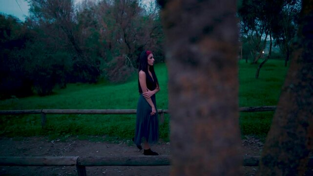 Chica joven caminando con miedo por un sendero en el bosque al caer la noche porque se cree que la siguen o vigilan.