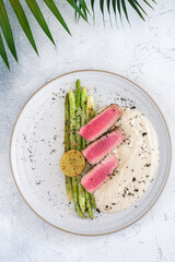 A top-down view of a gourmet dish featuring seared tuna slices, grilled lime, asparagus, and creamy puree, elegantly arranged on a white plate against