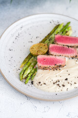 A gourmet dish featuring seared tuna slices, grilled lime, asparagus, and creamy puree
