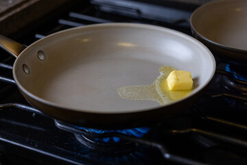 A pan with a piece of butter on it. The butter is melting and spreading out on the pan