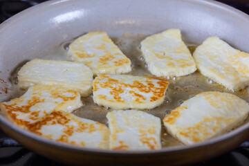 A pan of fried halloumi cheese is shown with a golden brown crust. cooking in hot butter. The dish looks delicious and inviting