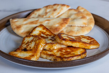 A plate of fried halloumi cheese with a side of pita bread. The food is golden brown and looks delicious.