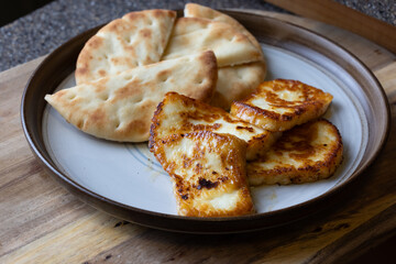 A plate of fried halloumi cheese with a side of pita bread. The food is golden brown and looks delicious.