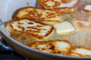 A pan of fried halloumi cheese is shown with a golden brown crust. cooking in hot butter. The dish looks delicious and inviting