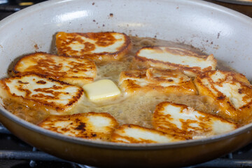 A pan of fried halloumi cheese is shown with a golden brown crust. cooking in hot butter. The dish looks delicious and inviting
