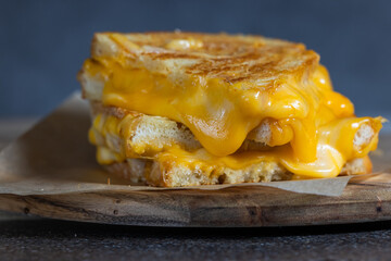 Grilled Cheese with melting cheese dripping from the inside. The sandwich is cut in half and placed on a wooden cutting board
