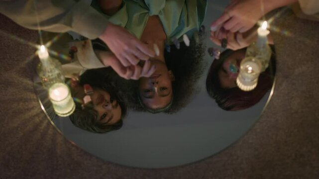 Mirror reflection of three multi-ethnic girls fortune telling with crystals and burning candles at night