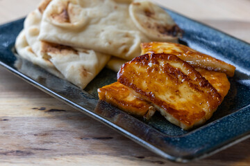 A plate of fried halloumi cheese with a side of pita bread. The food is golden brown and looks delicious.