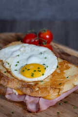 Croque Madame or Grilled cheese with ham and egg on a wooden cutting board. The sandwich is toasted and has a runny yolk