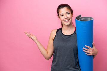 Young Brazilian sport woman going to yoga classes while holding a mat isolated on pink background...