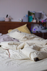 A cozy bedroom scene featuring an unmade bed with soft cream bedding and pillows, reflecting a...