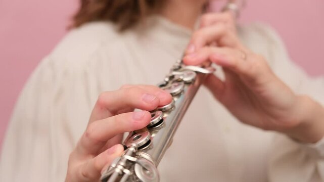 Close-up of hands playing a silver flute. Studio video on a soft pink background. Musical instrument performance. Music and art concept.