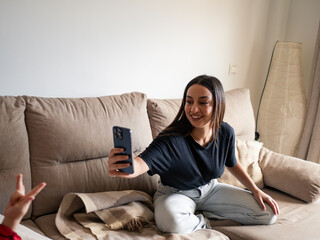 A young african woman smiles as she captures a picture of her son in her cozy living room. She sits...