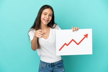 Young French woman isolated on blue background holding a sign with a growing statistics arrow...