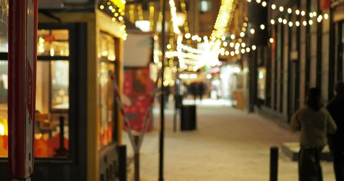 Holiday season. Out of focus. People walk along a brightly lit street at night under glowing garlands on a sidewalk covered with snow.  Siberia. Hand held.
