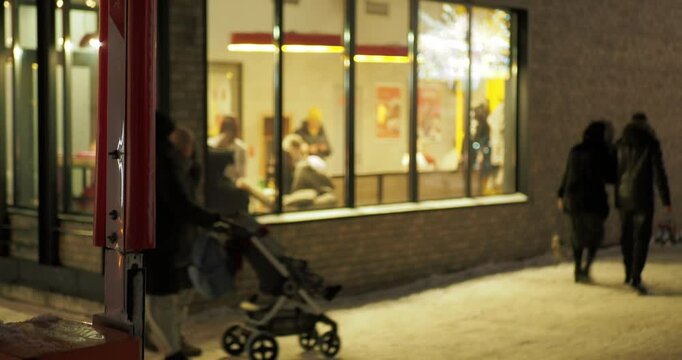 Night city, bokeh.  Novosibirsk. On a frosty evening, people walk along a sidewalk covered with snow past a brightly lit large window in which they can keep warm in the cold. Hand held. Siberia.