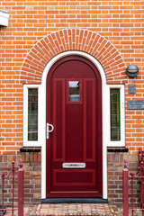 Fototapeta premium Wooden front door of a home. Front view of a wooden front door on a brick house with windows plants and a wide view of the porch and front walkway. Horizontal shot.