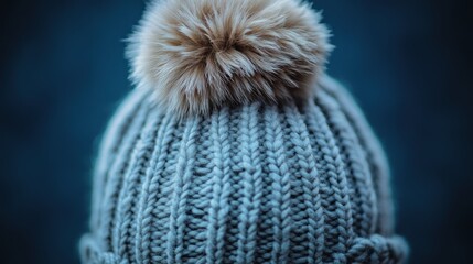 Close-up of a grey knitted beanie with a fluffy pompom.