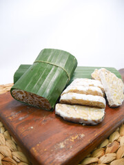 Close-up of traditional tempeh wrapped in banana leaves, with sliced pieces displayed on a wooden cutting board, isolated on a white background.  
