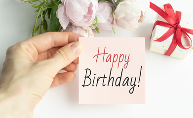 Happy birthday text on card in hand front of pink flowers.