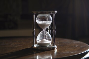 An elegant hourglass sits on a dark wooden table, symbolizing the passage of time and fleeting moments.