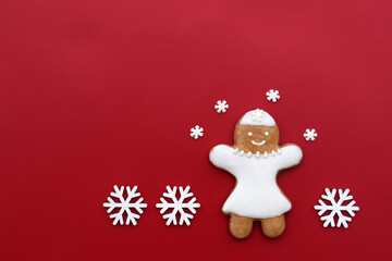 Smiling gingerbread woman on a red background with snowflakes around, copy space for text. Christmas time