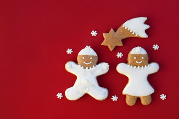 Smiling gingerbread man, woman and comet on a red background with snowflakes around, copy space for text. Christmas time