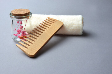 Wooden comb and a jar of pink flowers with a beige napkin on a gray background.