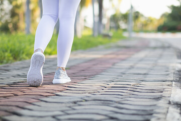 young woman wearing a sports outfit and sneakers walks along the path ahead towards her intended...