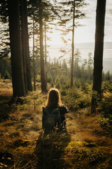 A woman is sitting in the middle of a serene forest with her backpack