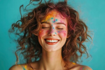 Delighted young woman with closed eyes smiling and shaking curly hair covering with multicolored paint against turquoise background 