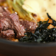 Close-up shot of a savory ramen bowl featuring succulent beef slices, seaweed, and vegetables, all immersed in a rich, flavorful broth and garnished with sesame seeds