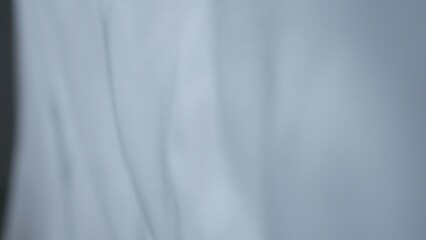 Transparent white silk soft fabrics floating with light shining through, shadows and shades reflected on the textile, close view.