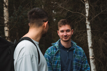 Two men are standing together in the lush woods talking to one another