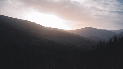 The sun shines beautifully through clouds over majestic mountains