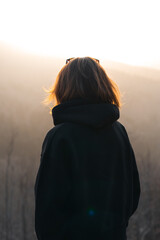 A woman dressed in a black hoodie is gazing thoughtfully at the sun