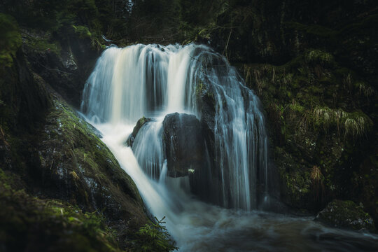 A beautiful and serene waterfall is surrounded by mossy rocks and trees nearby