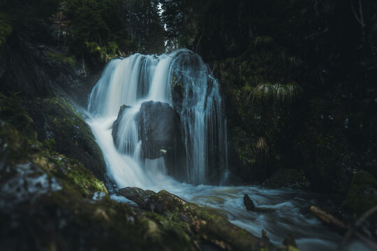 A beautiful and serene waterfall is surrounded by mossy rocks and trees nearby