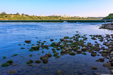 A river with a rocky shoreline and a city in the background