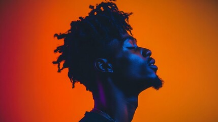Profile portrait of a young Black man with dreadlocks, illuminated by vibrant orange and purple light.