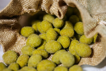 Close-up of vibrant yellow-green wasabi-coated nuts spilling out of a rustic burlap sack. Coated in a fine powder, they appear crunchy and flavorful.